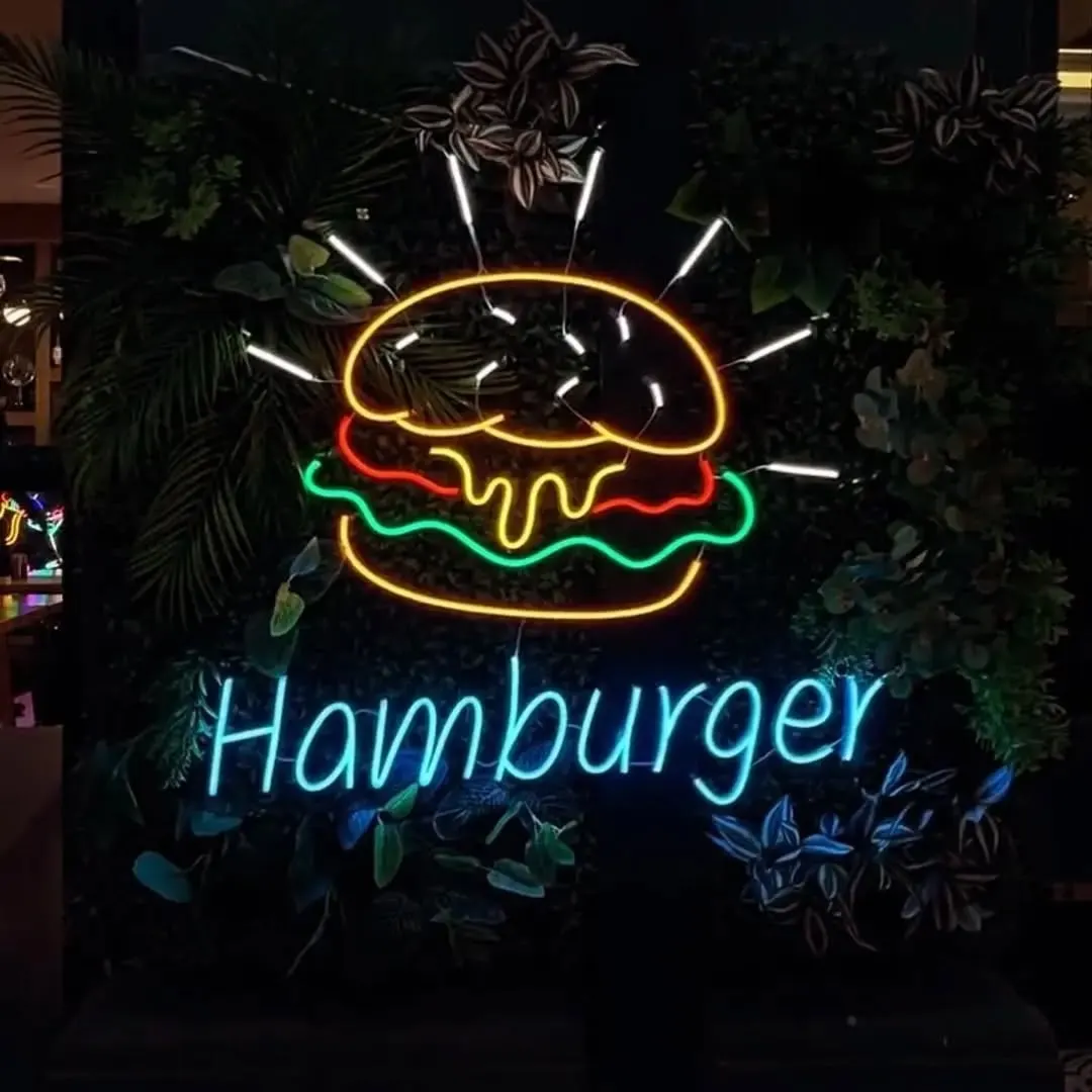 Bitki duvarında çok renkli hamburger ve mavi 'Hamburger' yazılı neon