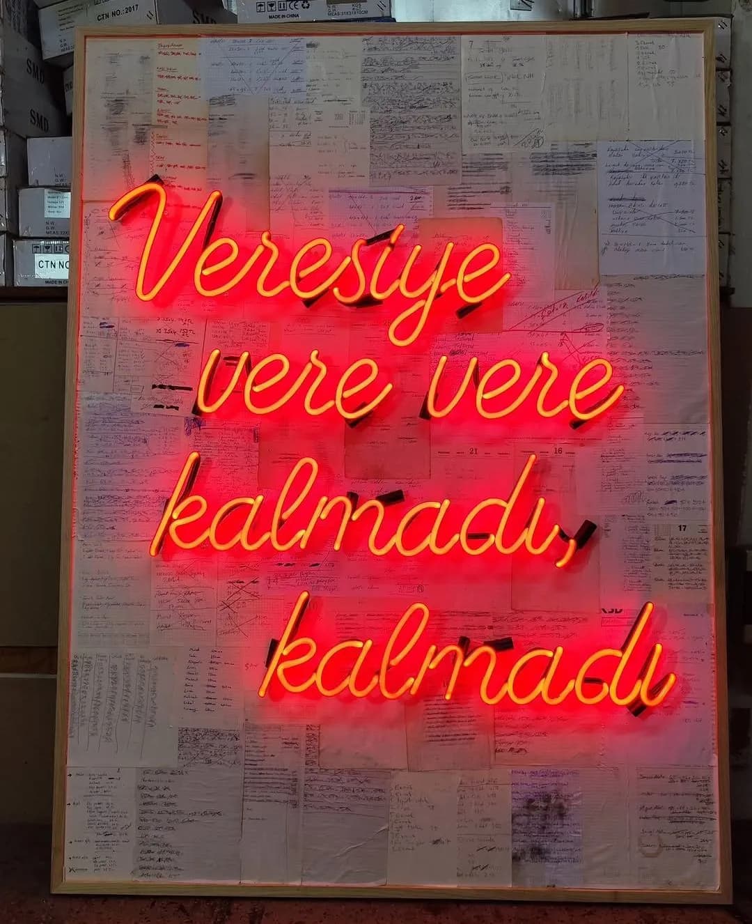 Red script 'Veresiye vere vere kalmadı' glass neon on a board of handwritten notes