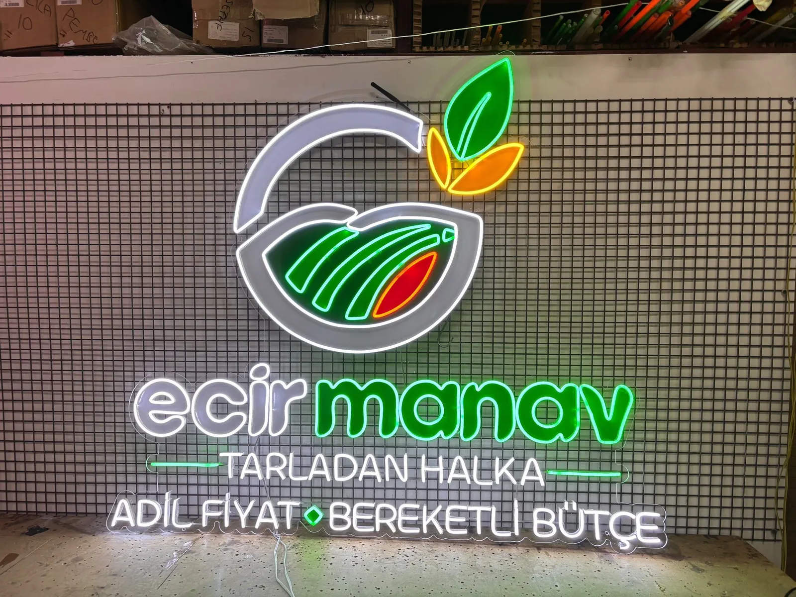 Green and white 'ecir manav' logo neon in the lit workshop