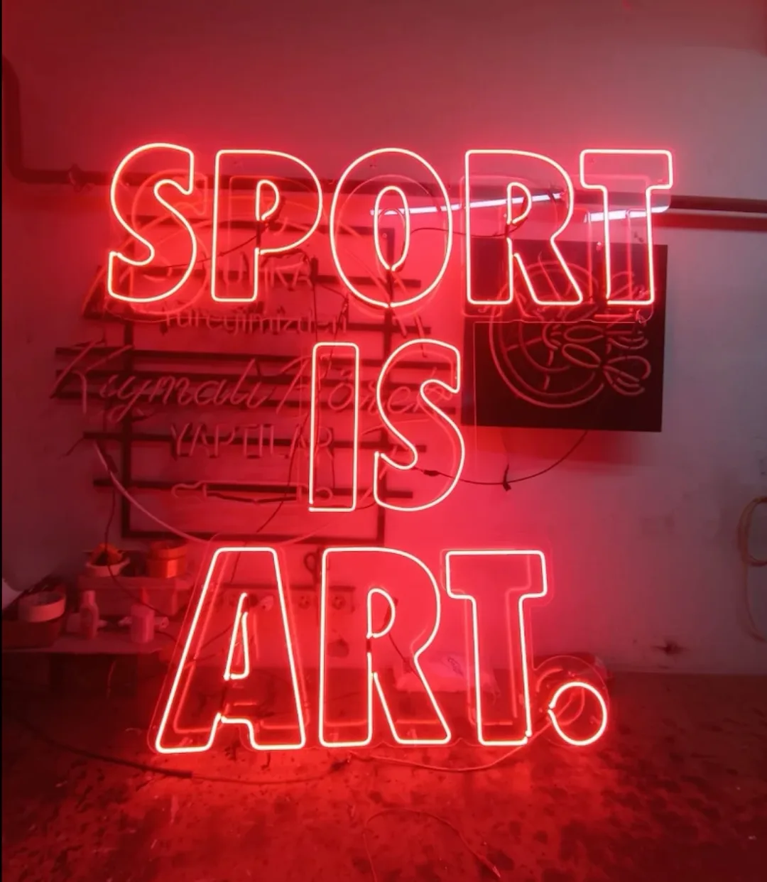 Red 'SPORT IS ART.' glass neon lettering on a workshop wall